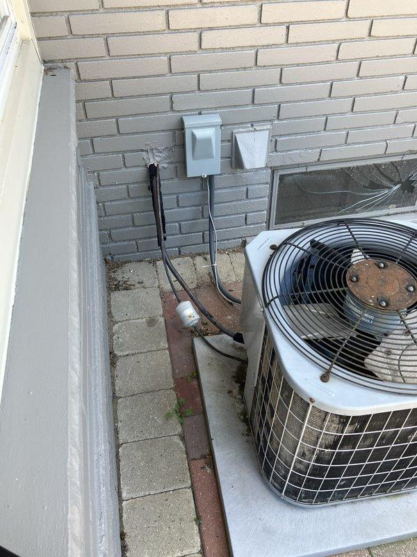 Conducted on-site evaluation for complete HVAC system replacement at residential property with 20-year-old equipment operating at minimal capacity. Assessed existing outdoor condensing unit positioned on concrete pad against brick exterior wall with dual electrical disconnect boxes, along with natural gas furnace located in basement. Documented current system configuration, electrical connections, and installation conditions to provide comprehensive replacement estimate for new air conditioning and heating equipment.