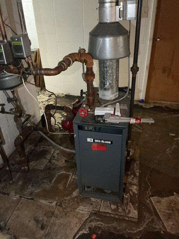 Conducted estimate on 35-40 year old Weil-McLain hot water boiler in basement that failed to provide adequate heating during previous winter season. Upon inspection, found extensive corrosion on piping system, water damage on concrete floor indicating previous leaks or flooding, and aging expansion tank with deteriorated connections. Documented existing mechanical room conditions including corroded brown piping, rusted fittings throughout the hydronic system, and overall equipment deterioration consistent with age and moisture exposure, then provided replacement recommendations for complete boiler system upgrade.