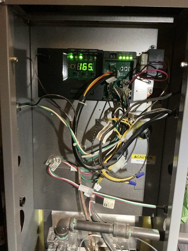 Completed annual hot water boiler inspection and tune-up on a 1-year-old 96,000 BTU/h natural gas unit located in utility room. Verified operational status of control board with digital display reading 165°F, inspected all electrical connections and wiring harnesses, and examined gas valve assembly and manifold components. All safety controls, warning labels, and AHRI-certified specifications confirmed in proper working order with no deficiencies noted.