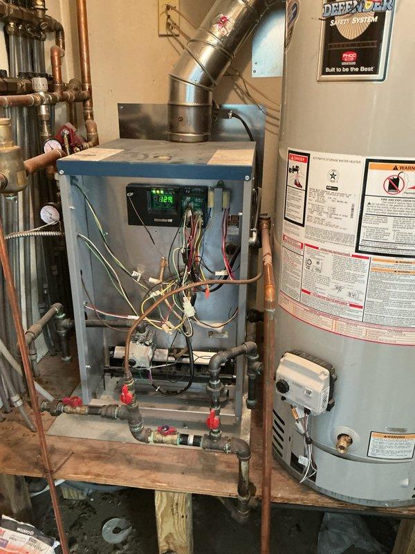 Completed comprehensive Gold boiler inspection on 3-year-old residential heating system located in garage. Performed full system evaluation including visual inspection of internal components with access panel removed, verified proper operation of control board and digital display, checked all electrical connections and wiring, inspected gas lines and copper piping connections, tested safety shut-off valves, examined ductwork and venting system, and assessed expansion tank mounting. Inspected associated water heater and plumbing manifold system with multiple zone valves. All components found to be operating within normal parameters with no immediate service needs identified. Documentation photos captured for maintenance records.