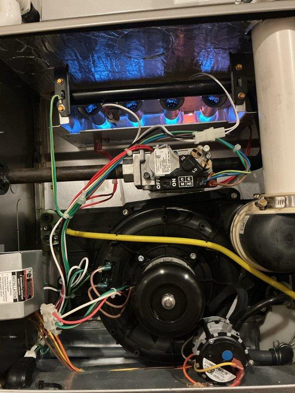 Completed comprehensive Gold-level furnace inspection and tune-up on a 4-year-old unit located in basement. Performed full system evaluation including burner assembly inspection with flames burning clean and blue, indicating proper combustion and air-fuel mixture. Verified gas valve operation and all electrical connections secure with proper wire routing. Inspected blower motor assembly and confirmed operational integrity. Checked UV light system functioning correctly in upper cabinet section. Examined all control components, safety switches, and wiring harnesses for wear or damage. Verified condensate drainage system clear and PVC vent piping secure. Confirmed all manufacturer labels and warning decals present and legible. System operating within normal parameters with no deficiencies noted. Unit maintained preventive maintenance schedule and remains in good working condition with no repairs required at this time.