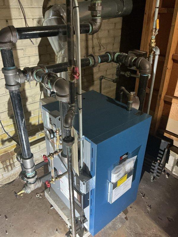 Completed comprehensive Gold Boiler Inspection on a 3-year-old steam boiler system located in basement. Performed thorough visual examination of boiler unit, verified operational status, and inspected all associated piping network including supply and return lines with multiple zone valves. Checked all red-handled isolation valves for proper operation, examined insulated pipe sections for integrity, and verified secure mounting and connections throughout the distribution system. Inspected control panel display and safety labels on boiler unit, confirmed proper thermostat operation showing 70°F setting on PRO1 programmable unit, and documented system configuration with photographic records. All components found to be functioning properly with no immediate service needs identified.