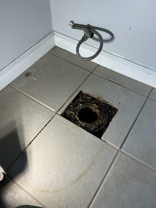 Responded to a water leak originating from the main drain pipe located beneath the toilet. Upon inspection, discovered severely corroded cast iron drain piping in the basement ceiling area showing extensive rust deterioration and active moisture damage. Removed floor tiles in the bathroom to access the toilet flange and underlying drain connection, exposing the compromised pipe section. Documented the extent of corrosion on the main drain stack and assessed the structural integrity of surrounding plumbing components, including the hot and cold water supply lines running adjacent to the affected area.