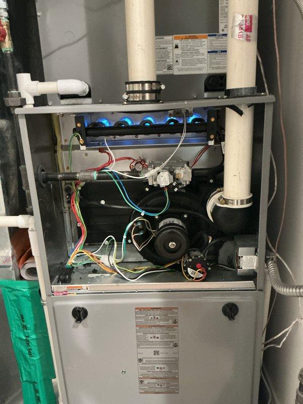 Completed comprehensive Gold Furnace Inspection on two forced-air heating units, including a 2-year-old furnace located on the lower level and a second unit on the second floor. Performed full system evaluation with equipment operational at time of service. Verified proper burner ignition and flame characteristics, observing consistent blue flame pattern across all five burners in combustion chamber. Inspected thermostat operation, confirming digital Honeywell Home ProSeries unit displaying accurate temperature and humidity readings at 72°F and 60% humidity. Examined all internal components including draft inducer motor, gas valve assembly, electrical connections, and control board wiring. Verified proper operation of PVC venting and condensate drainage systems. Documented system condition through photographic records showing active burner operation and thermostat functionality. Both furnace units confirmed operational with no immediate service requirements identified during inspection