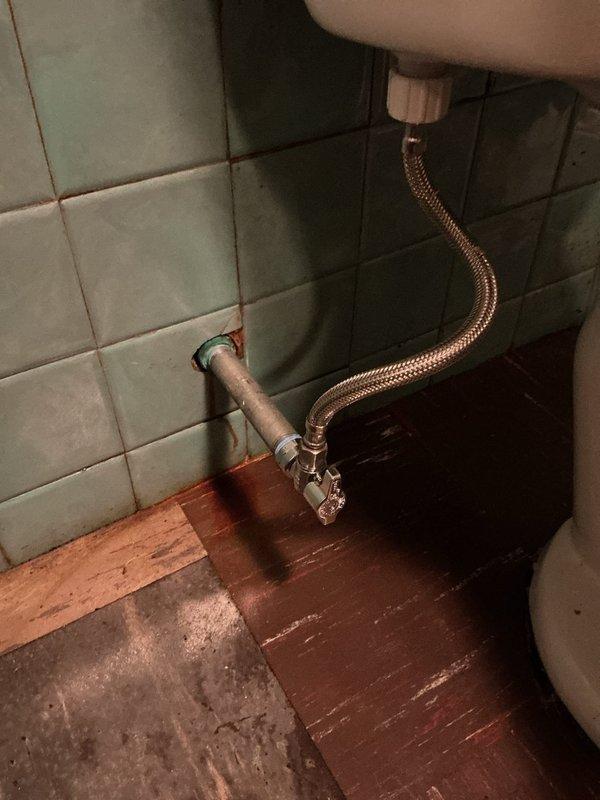 Responded to call for leaking water supply line between wall shut-off valve and toilet. Upon arrival, found corroded pipe connection at wall penetration with visible rust staining on surrounding tile and active leak at escutcheon. Shut off main water supply, removed deteriorated flexible supply line, and replaced with new braided stainless steel connector. Verified proper seal at wall connection and toilet tank inlet. Restored water supply and tested system under full pressure with no leaks detected.