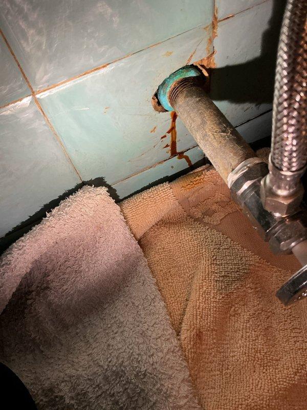 Responded to call for leaking water supply line between wall shut-off valve and toilet. Upon arrival, found corroded pipe connection at wall penetration with visible rust staining on surrounding tile and active leak at escutcheon. Shut off main water supply, removed deteriorated flexible supply line, and replaced with new braided stainless steel connector. Verified proper seal at wall connection and toilet tank inlet. Restored water supply and tested system under full pressure with no leaks detected.
