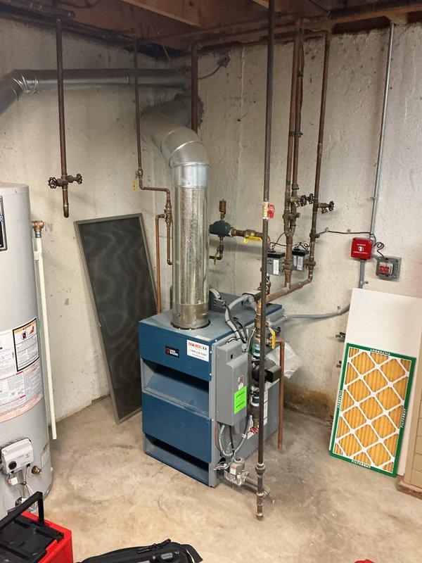 Completed comprehensive Gold furnace inspection on an 8-year-old boiler system located in basement. Performed thorough visual examination of blue metal boiler unit, expansion tank, and associated heating components. Inspected all copper piping connections, shut-off valves, and pressure gauges throughout the system for proper operation and potential leaks. Evaluated water heater connections and temperature/pressure relief valve configuration. Checked galvanized ductwork connections and mounting integrity of expansion tank. Assessed condition of black vertical pipes, noting visible corrosion and mineral buildup on one section that will require monitoring. Verified proper installation of pipe hangers and support systems throughout mechanical room. Examined HVAC air filter condition and accessibility. All equipment currently operational with no immediate service requirements identified. System functioning within normal parameters at time of inspection.