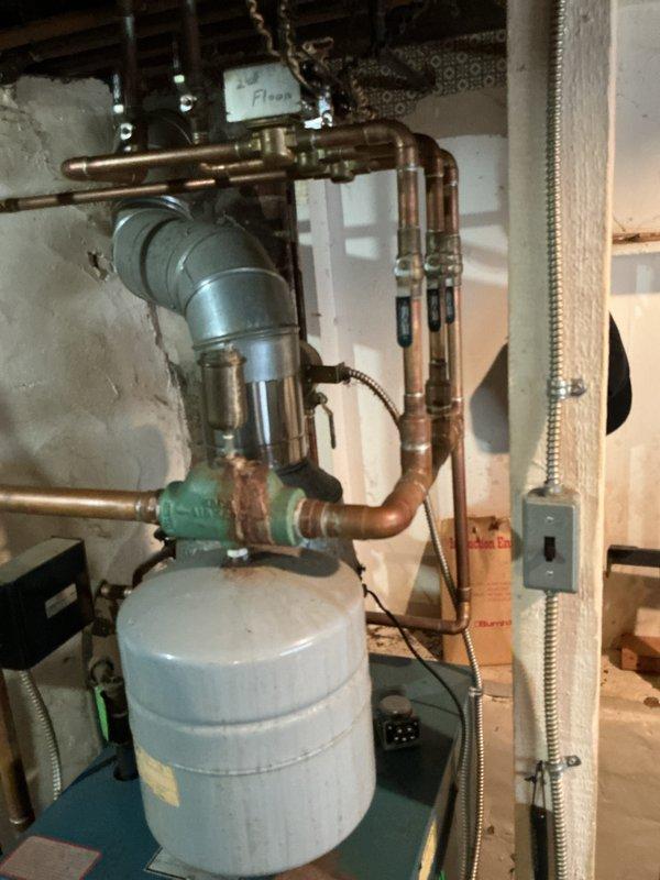 Provided estimate for hot water boiler replacement in basement mechanical room. Existing system is very old with malfunctioning controls that prevent proper shutdown, presenting safety and efficiency concerns. Current installation includes aged copper piping with significant patina, multi-zone heating distribution system with floor-designated controls, expansion tank, and circulation pumps showing considerable wear from years of operation.