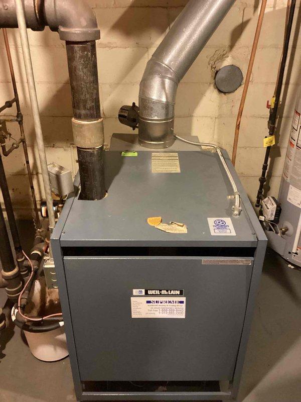 Completed residential boiler maintenance inspection on a Weil-McLain heating unit located in basement mechanical room. Inspected hydronic heating system including copper piping connections, venting system, and thermostat operation, verifying unit is functioning properly for continued residential heating service.