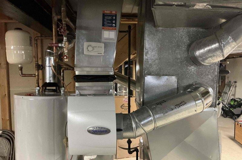Installed Aprilaire 600M bypass humidifier system in residential basement mechanical room. Unit was mounted adjacent to existing furnace with proper electrical and water supply connections, including copper piping with shutoff valve and drain line installation to integrate with the forced air heating system.
