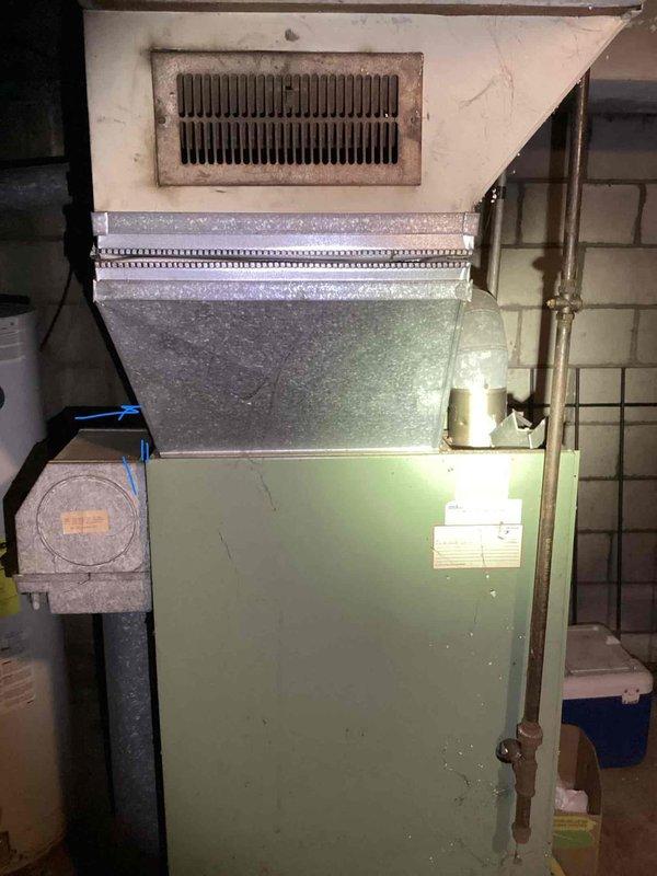 Conducted comprehensive assessment of basement-installed furnace system experiencing failure symptoms from previous winter, including intermittent clicking and startup issues. Upon inspection, determined existing unit was aged beyond economical repair with compromised internal components, deteriorated wiring connections, and worn blower assembly visible through access panel. Provided detailed estimate for complete furnace replacement including removal of existing green-cabinet unit, installation of new high-efficiency heating system, proper venting modifications, and integration with existing ductwork and air handler components. Documented current system configuration including copper refrigerant lines, metal supply grate, and flue pipe assembly to ensure accurate equipment sizing and compatibility for replacement installation.