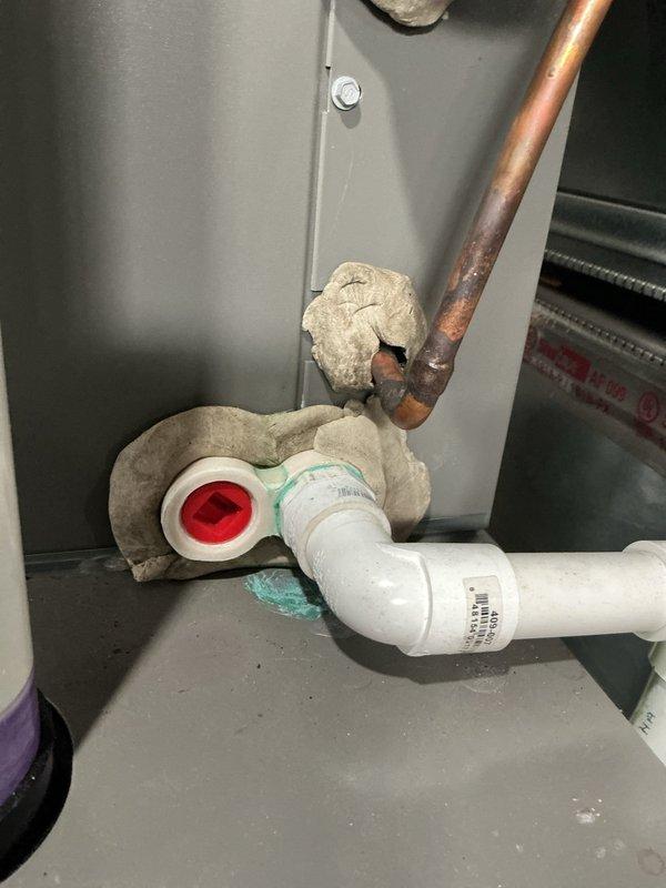 Responded to service call for 2-year-old forced air AC system in basement producing loud humming noise and green fluid leak from piping. Created 90-degree bends in refrigerant line set to proper routing configuration. Inspected indoor evaporator coil assembly and PVC condensate drain system where green-tinted condensate was discharging through drain line with red cap fitting. Examined outdoor condensing unit on concrete pad with insulated refrigerant lines entering building through exterior wall. Verified proper line set insulation installation on copper refrigerant piping and confirmed system connections at both indoor and outdoor units. Addressed refrigerant line routing concerns and resolved drainage issue.