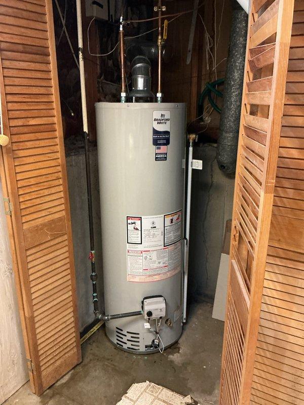 Completed installation of a standard 40-gallon Bradford White gas water heater in residential utility closet. Unit was properly positioned, connected to existing copper supply lines, equipped with expansion tank and pressure relief valve, and all gas connections were made with Honeywell gas control system featuring pilot ignition and temperature regulation. All plumbing connections were secured, system was tested for proper operation, and installation meets code requirements.