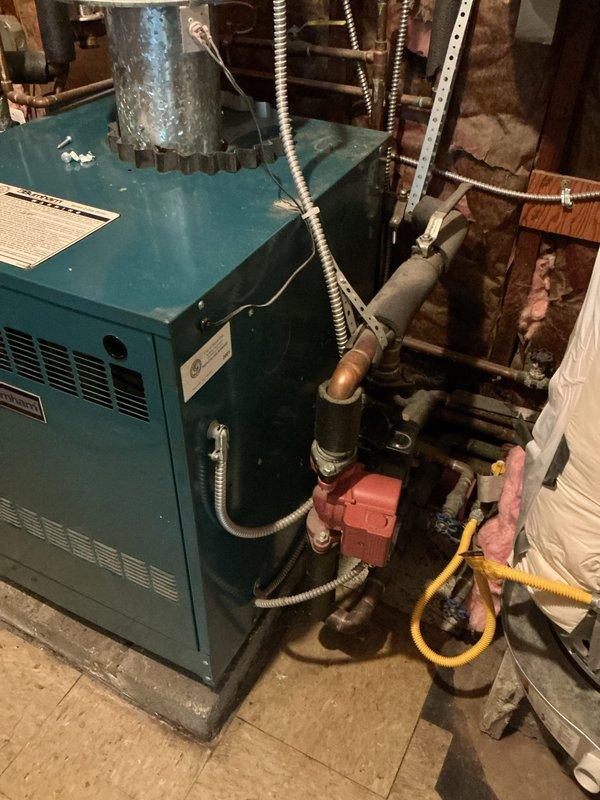 Completed comprehensive inspection and evaluation of 10+ year old boiler system located in utility room. Assessed condition of teal-colored boiler unit, associated piping infrastructure including copper lines with protective wrapping, red circulation pump assembly, yellow flexible gas line connections, and cylindrical expansion tank mounted on wall studs. Evaluated all mechanical components, ventilation systems, flexible conduits, and pressure vessel for replacement recommendation. Documented existing equipment configuration and provided estimate for complete system replacement based on age and condition of current heating plant.