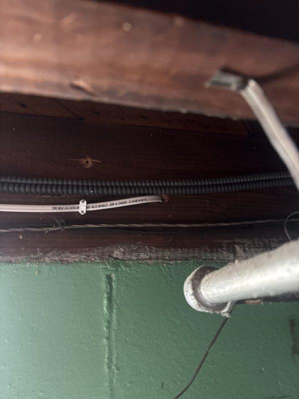 Completed electrical service repair involving installation and routing of new electrical wiring through ceiling joists and structural cavities. Installed exterior-mounted electrical junction box with weatherproof conduit on brick wall near glass block window, ensuring proper grounding and code-compliant installation for outdoor fixture or outlet connection.