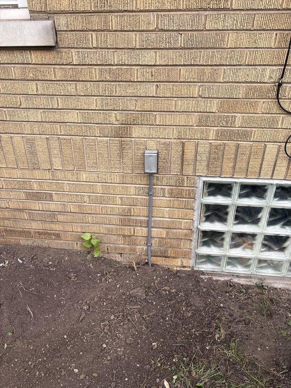 Completed electrical service repair involving installation and routing of new electrical wiring through ceiling joists and structural cavities. Installed exterior-mounted electrical junction box with weatherproof conduit on brick wall near glass block window, ensuring proper grounding and code-compliant installation for outdoor fixture or outlet connection.
