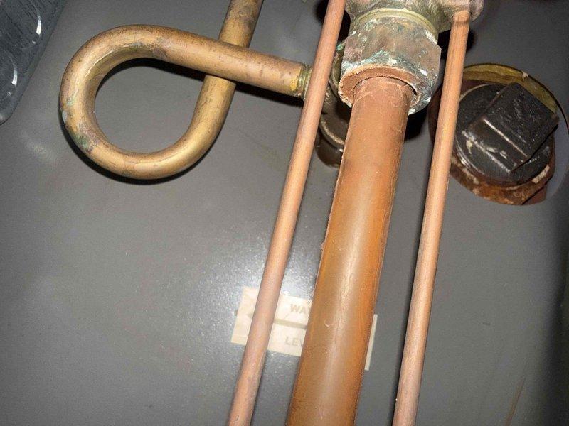 Completed comprehensive tune-up inspection on 10+ year old HVAC system located in basement, including full evaluation of furnace, humidifier, thermostat, and hot water tank components. Documented significant rust corrosion at base of equipment support structure where metal post contacts concrete floor, requiring attention to prevent structural integrity issues. Observed aged copper plumbing with visible oxidation, green patina formation, and corrosion on water lines and brass fittings throughout the system.