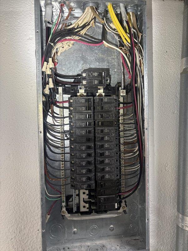 Completed comprehensive electrical panel inspection for city compliance on 20-year-old residential system. Performed thorough examination of main distribution panel containing approximately 20-24 circuit breakers arranged in dual columns, verified proper wire connections and color coding throughout, inspected all incoming conductors from overhead ceiling cavity, and documented panel condition with detailed photography. All breakers, wiring terminations, and panel enclosure found to be accessible and properly secured for municipal inspection approval.