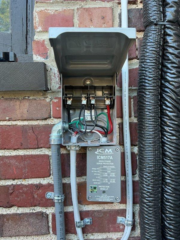 Responded to service call for mini split system displaying U4 error code with no heating or cooling capability on unit installed within past year. Upon arrival, inspected outdoor condenser unit and electrical disconnect box mounted on exterior brick wall. Diagnosed communication fault between indoor and outdoor units causing U4 error. Verified all electrical connections at disconnect box, checked circuit breakers, and inspected line set connections. Tested surge protection device labeled ICM517A for proper operation. Cleared error code, restored system communication, and verified unit returned to normal heating and cooling operation. System tested and confirmed fully operational upon departure.