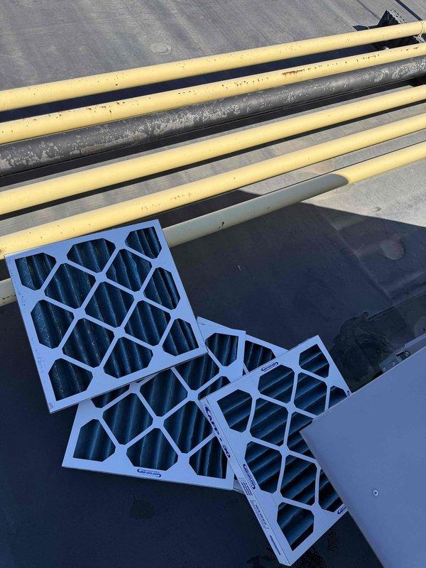 Completed scheduled filter change on commercial rooftop unit requiring lift access. Removed and replaced multiple pleated air filters in the RTU's filter rack system, installing three new filters on the unit exterior and four filters within the 2x2 configuration filter housing. All filters were properly secured with mounting clips and verified for correct fitment to ensure optimal airflow and system efficiency.