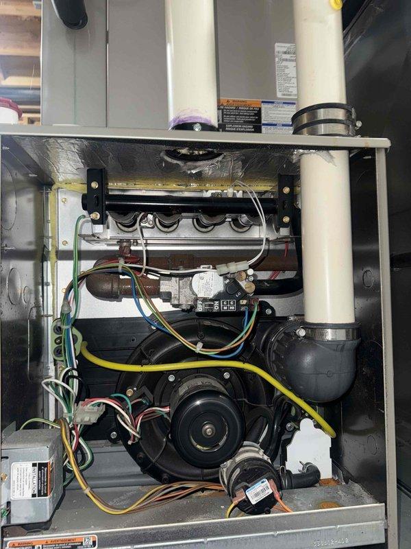 Responded to service call for 11-year-old forced air furnace in basement not producing warm air with thermostat temperature dropping below setpoint. Arrived on-site before 9 AM as requested and contacted customer prior to arrival. Performed diagnostic inspection of furnace system, removing access panel to examine internal components including blower motor assembly, control board, heat exchanger, and electrical connections. Verified all wiring connections at blower motor (yellow, green, red, and white leads) were secure and properly terminated. Inspected control board operation and associated wiring harness for any signs of failure or loose connections. Examined heat exchanger assembly for proper operation and checked condensate drain lines (white PVC piping) for blockages or restrictions. Assessed blower motor functionality and verified proper electrical supply to all system components. Documented equipment condition through photographs showing internal mechanical and electrical compon