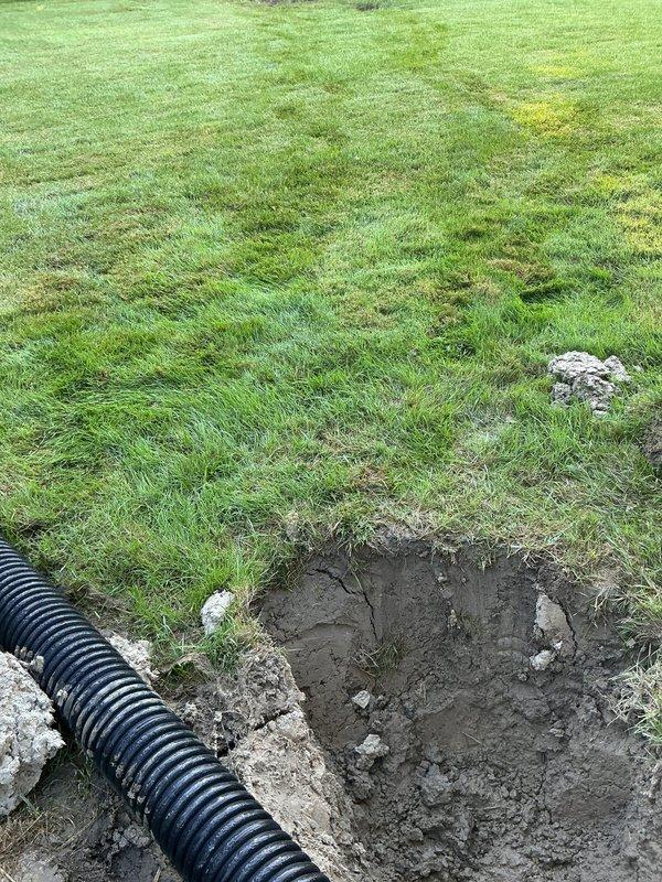 Responded to a sump pump discharge line issue where water was spitting out through the vent and causing exterior leakage. Upon inspection, confirmed the discharge line was clogged, preventing proper water flow from the basement sump pump system. Excavated and cleared the obstruction from the exterior drainage system, which included black corrugated perforated drainage pipes running from the foundation. Restored proper water flow through the discharge line and verified the sump pump was operating correctly with no further leakage at the vent or exterior discharge point.