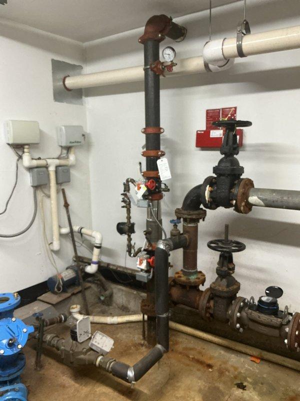 Responded to commercial backflow preventer failure in mechanical room. Upon inspection, identified two faulty backflow prevention assemblies exhibiting active leakage and one inoperable gate valve. The backflow devices showed significant corrosion on valve bodies, flanges, and internal components, compromising their ability to maintain proper check valve function and prevent reverse flow contamination. The non-turning valve displayed seized operation due to mineral buildup and deteriorated internal mechanisms. Documented existing plumbing configuration including corroded gate valves, pressure gauges, and interconnected piping systems. Photographed current conditions of both backflow assemblies and surrounding infrastructure to support repair recommendations and compliance requirements for commercial cross-connection control.