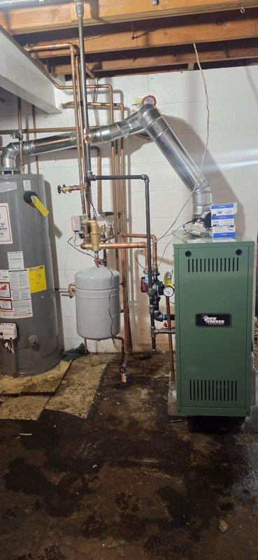 Completed full boiler installation in basement mechanical room, including green residential boiler unit with associated copper piping network, expansion tank, pressure gauges, brass valves, and metallic exhaust venting system. Installation included three thermostats and hydronic heating system connections to existing water heater. Mechanical, boiler, and reconnection permits were requested, with electrical contractor scheduled to return for final boiler wiring to complete the installation.