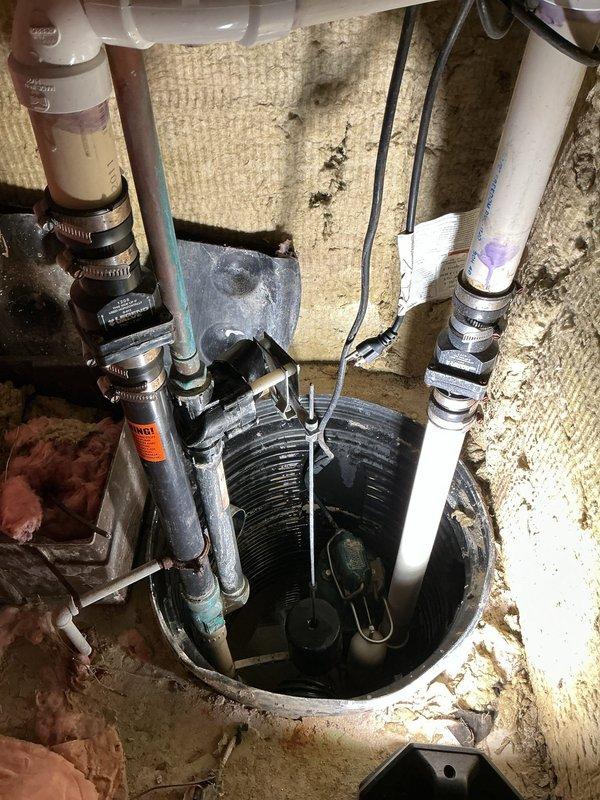 # Sump Pump Leak Repair

Responded to service call for reported sump pump leak in basement area. Upon arrival, conducted thorough inspection of existing sump pump system installed in circular black basin set into concrete floor. Examined submersible pump unit, discharge piping configuration, and all connection points for signs of water seepage.

Inspected multiple PVC discharge lines including white and beige pipes secured with metal hose clamps, noting age-related wear and discoloration on existing plumbing components. Traced all piping connections from pump basin through overhead plumbing infrastructure, including P-trap assembly and corrugated flexible discharge line. Evaluated pipe joints, coupling connections, and clamp integrity throughout the system.

Identified source of leak at connection point and performed necessary repairs to eliminate water seepage. Tested pump operation through multiple cycles to verify proper function and confirm leak resolution. Checked float switch mec