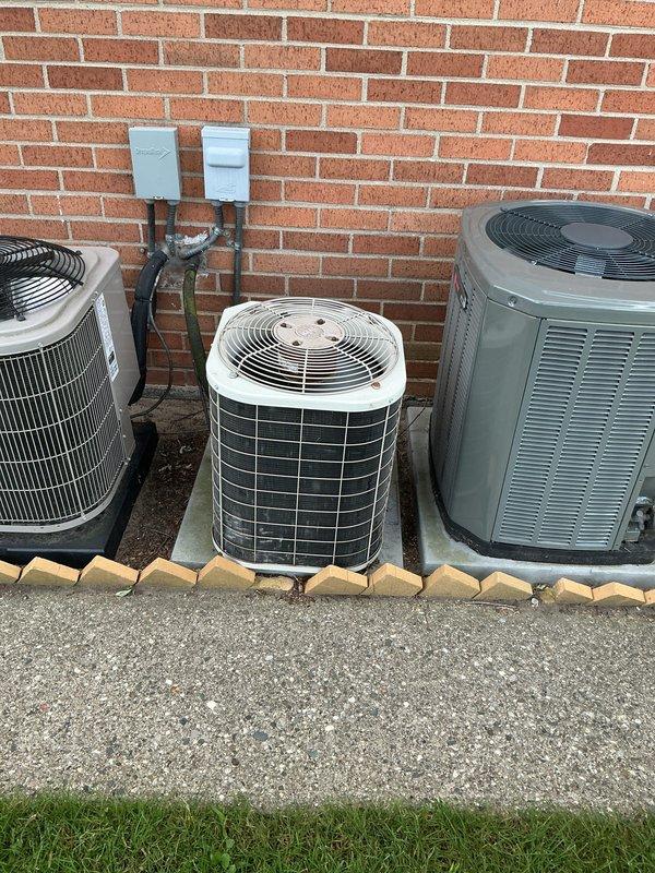 Conducted comprehensive inspection of 2003 Bryant furnace system located in basement condo unit and identified failed heat exchanger requiring immediate replacement. Provided full HVAC system replacement estimate including new furnace, air handler, and associated components to ensure safe and efficient operation. Documented existing installation configuration with white PVC condensate drain lines, humidifier integration, and electrical connections, as well as exterior condensing units positioned on concrete pads against brick wall for complete system assessment.