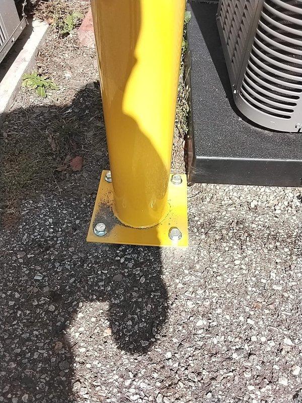 Installed yellow safety bollards around exterior HVAC units to comply with mechanical code violation identified during inspection. Three condensing units were protected with properly anchored bollards mounted on concrete pads with base plates and bolts, creating physical barriers against potential vehicular damage. Installation meets required safety standards and resolves the outstanding code compliance issue.