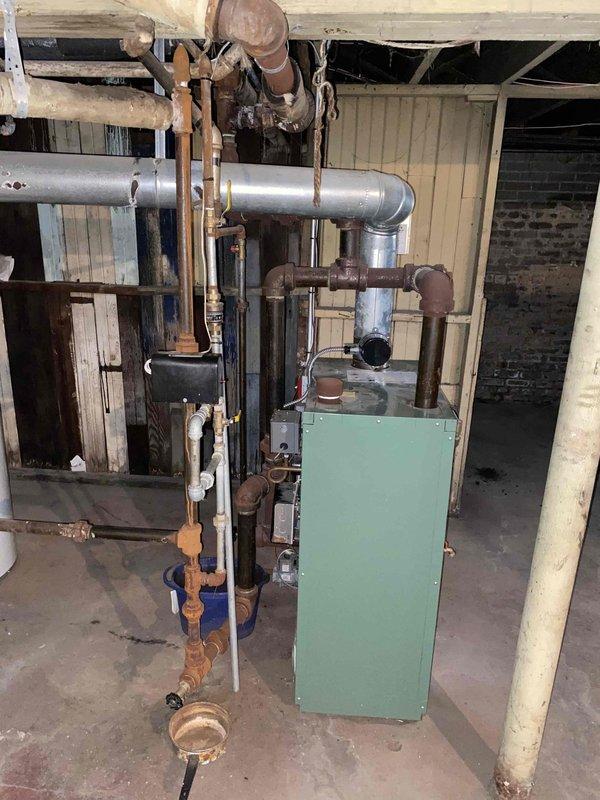 Responded to no heat complaint on 10-year-old boiler system located in basement. Upon inspection, found extensive corrosion and oxidation on copper piping throughout the heating system, with visible deterioration on vertical pipe runs, joints, and fittings. Noted active leak requiring bucket placement for water collection, with floor staining indicating ongoing moisture issues. Circulator pump, gas valve assembly, and associated piping connections showed significant age-related wear. Due to the extent of corrosion, compromised piping integrity, and safety concerns with the aging system components, provided comprehensive estimate for boiler replacement and associated piping upgrades to restore reliable heating operation.