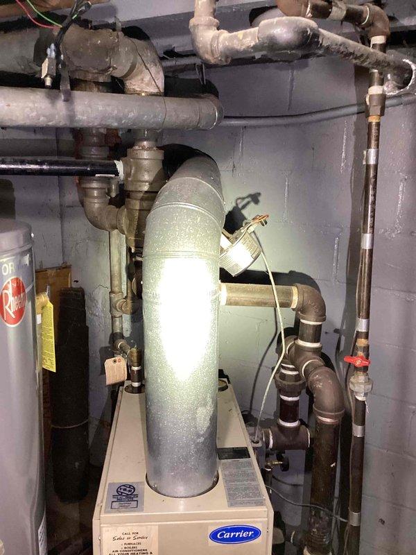 Conducted estimate for replacement of 31-year-old natural gas steam boiler system that has been experiencing frequent operational failures and shutdowns. Existing Carrier unit with expansion tank, associated piping, and steam radiator distribution system was evaluated in mechanical room. All radiators currently functional but technician has previously recommended full system replacement due to reliability issues and age of equipment.