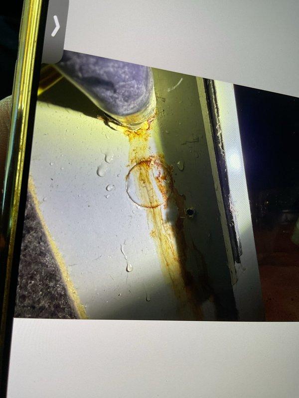 Responded to service call for reported furnace leak on 10+ year old forced air system located in basement. Upon inspection, discovered significant corrosion and rust staining on condensate drain line and equipment housing, indicating active water leakage from the condensate drainage system. The black PVC elbow connector showed evidence of moisture accumulation with visible water droplets on surrounding surfaces and extensive orange-brown rust deposits flowing down the white exterior panel of the furnace cabinet. Documented the deteriorated condition with photographs showing the corroded pipe connection point and resulting water damage to the equipment housing. The rust staining patterns and moisture presence confirmed ongoing condensate drainage issues requiring immediate attention to prevent further corrosion damage to the furnace cabinet and surrounding components.