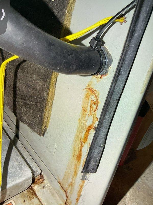 Responded to service call for reported furnace leak on 10+ year old forced air system located in basement. Upon inspection, discovered significant corrosion and rust staining on condensate drain line and equipment housing, indicating active water leakage from the condensate drainage system. The black PVC elbow connector showed evidence of moisture accumulation with visible water droplets on surrounding surfaces and extensive orange-brown rust deposits flowing down the white exterior panel of the furnace cabinet. Documented the deteriorated condition with photographs showing the corroded pipe connection point and resulting water damage to the equipment housing. The rust staining patterns and moisture presence confirmed ongoing condensate drainage issues requiring immediate attention to prevent further corrosion damage to the furnace cabinet and surrounding components.