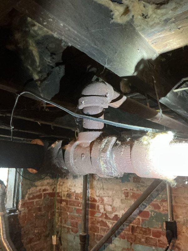 Conducted on-site assessment of steam boiler piping system requiring replacement. Inspected deteriorated threaded pipe connections and aging distribution lines running through basement ceiling joists, noting surface corrosion and wear on existing piping. Evaluated ceiling damage above work area and documented exposed brick foundation walls, structural framing, and routing of existing mechanical systems to provide comprehensive estimate for complete pipe replacement connected to steam boiler unit.