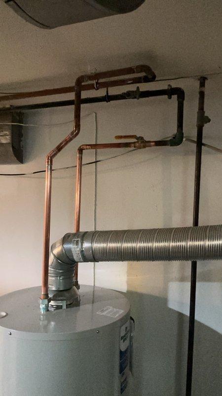 Completed installation of replacement tanked water heater in basement utility area with extended venting system. Due to the exceptionally long venting run required for this installation, additional venting materials were utilized to properly exhaust combustion gases from the unit. The installation included connecting flexible metallic ductwork with rigid metal elbows to accommodate the extended horizontal run across the ceiling space, ensuring proper draft and code compliance. All water supply connections were completed using existing copper piping infrastructure, and the unit was reconnected to the distribution system. The water heater was positioned and secured in accordance with manufacturer specifications and local plumbing codes. Final installation includes fully operational venting system with appropriate pitch and support, restored water service, and verified proper operation of all mechanical components.