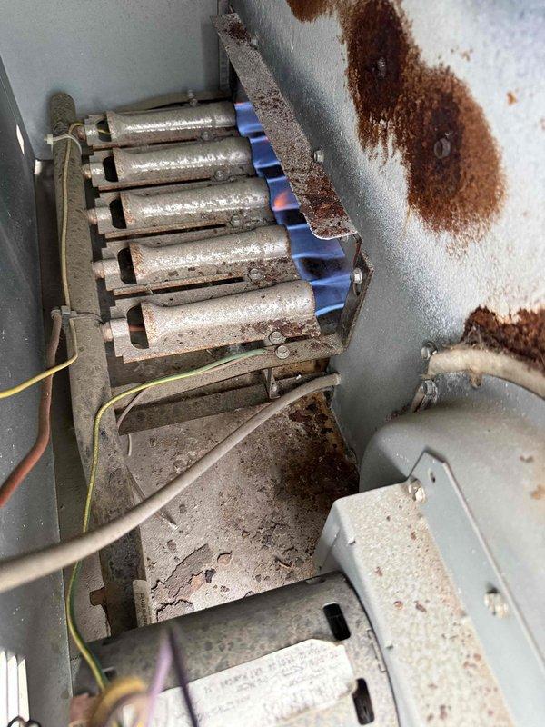 Completed fall maintenance on commercial rooftop unit. During inspection, discovered significant frost buildup on refrigerant lines and ductwork indicating possible insulation failure or refrigerant issue requiring further evaluation. Heat exchanger inspection revealed active blue flames with proper combustion, however extensive rust and corrosion present throughout cabinet interior and on heat exchanger surfaces, suggesting prolonged moisture exposure and potential unit degradation that may compromise system longevity and efficiency.