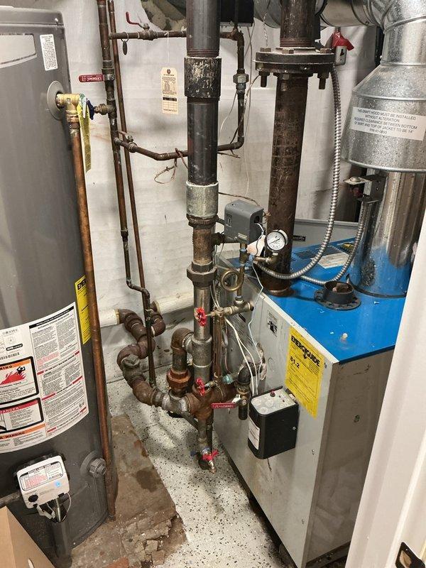 Completed Gold-level maintenance inspection on residential steam boiler system. Performed comprehensive visual examination of boiler components, associated piping, valves, and pressure controls. Inspected water heater, circulation system, pressure vessel, and all interconnected mechanical equipment in basement mechanical room. Noted visible corrosion and oxidation on multiple pipe sections and threaded fittings throughout the system, particularly on horizontal runs and valve connections. Documented condition of red-handled gate valves, pressure gauge, control box, and copper piping. System operational at time of inspection; photographed equipment conditions for maintenance records.