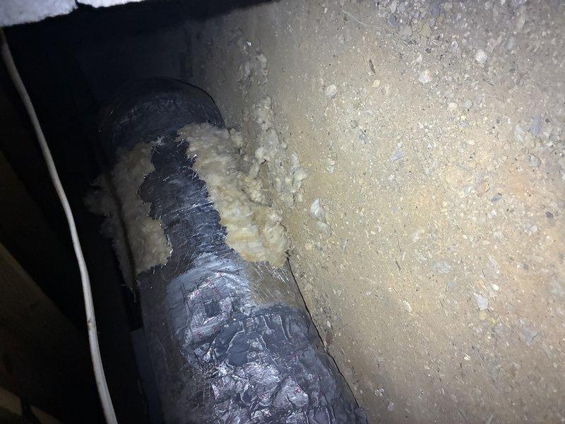 # SASC Protection Visit - No Cooling Issue

Responded to service call for SASC unit not cooling, system approximately 5 months old. Conducted comprehensive Protection Visit inspection to diagnose cooling failure and assess overall system condition.

Upon arrival, performed visual inspection of accessible ductwork and HVAC components. Documented flexible duct penetration through structural surface with spray foam insulation applied at entry point. Observed standard installation practices with corrugated flexible ducting passing through concrete or drywall surface in what appears to be attic or crawl space area. Insulation material properly sealed around duct penetration to prevent air leakage and maintain energy efficiency.

Inspected basement or crawl space area where additional ductwork components are located. Noted silver reflective flexible duct running vertically along wall corner with foil-faced insulation wrap. Documented significant wall deterioration with extensive peeling pain