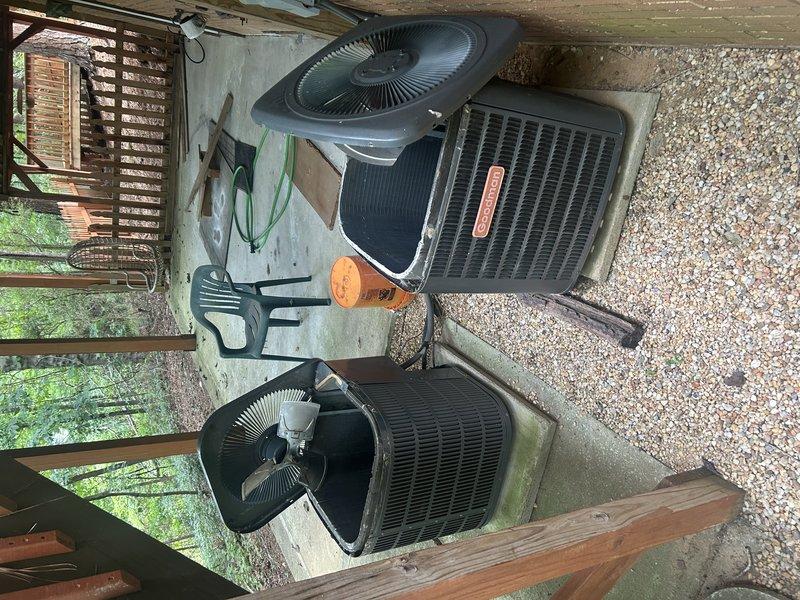 Completed initial protection plan visit for two outdoor HVAC condensing units installed beneath covered structure. Performed comprehensive visual inspection of both systems, documenting equipment condition and operational status through photographic documentation. Inspected first unit's internal components including compressor assembly, electrical connections, refrigerant lines, and condenser coil with radial fin configuration. Verified proper wiring connections with color-coded leads secured to compressor. Examined braided refrigerant lines and copper tubing connections for signs of wear or damage. Assessed second unit's exterior condition and fan grille assembly. Noted environmental factors affecting installation area including moisture presence, algae growth on concrete pads, and weathering of surrounding deck structure. Both units appear operational with normal wear patterns consistent with outdoor exposure. Equipment positioned on concrete pads with adequate clearance for airflow 