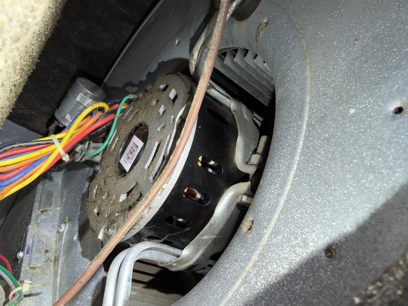 Completed drive-by inspection of HVAC unit and documented equipment condition through photographic assessment. Visual examination revealed unit identification labels, QR code, and manufacturer specifications on exterior casing, along with internal blower motor assembly showing significant dust accumulation on motor housing and surrounding components. Observed multiple electrical connections, copper refrigerant line, and finned heat sink component, all exhibiting operational wear and debris buildup consistent with equipment requiring maintenance attention.
