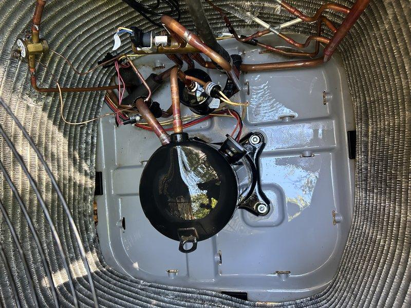 Completed routine service agreement maintenance visit on outdoor heat pump system. Performed comprehensive inspection of condenser unit exterior and internal components. Verified proper operation of compressor, examined refrigerant lines for leaks or damage, and inspected electrical connections including wiring and terminal points. Checked fan motor operation and blade condition through protective grille. Assessed unit mounting stability and clearance from surrounding vegetation and building foundation. Documented equipment condition through photographic record showing exterior housing with perforated ventilation grilles and internal view of compressor assembly, copper refrigerant piping, and electrical wiring harness. Noted debris accumulation around base of unit from seasonal leaf fall. System operating within normal parameters under existing warranty coverage without ultraviolet light component.