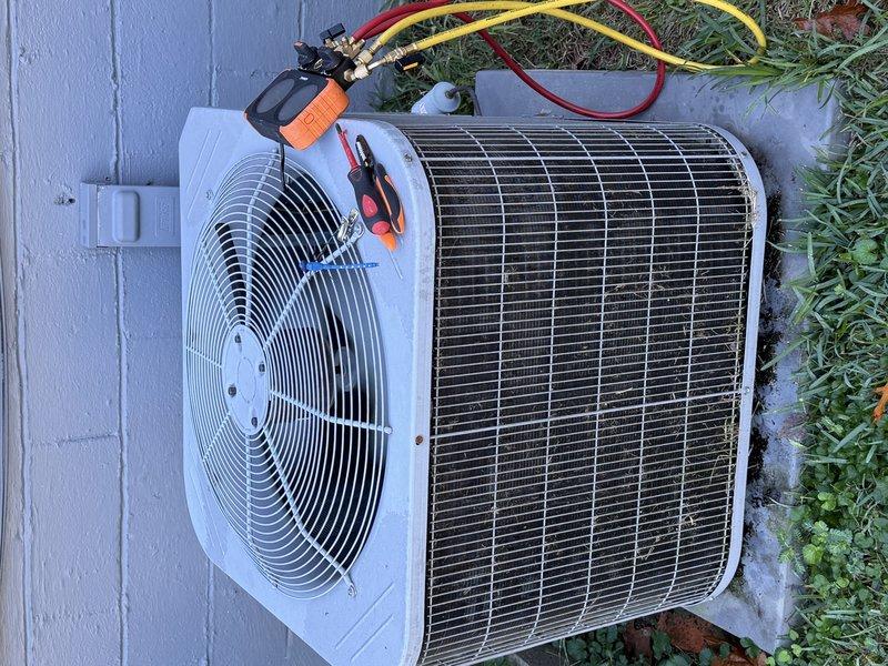 Performed a Service Agreement maintenance visit on the heating and cooling system, connecting a digital manifold gauge set to the outdoor condenser to check refrigerant pressures and overall system performance. Inspected the condenser and found the coil heavily fouled with dirt, grass clippings, and leaf debris restricting airflow; cleared the debris from the coil guard and fins to restore proper heat transfer and airflow. Verified the electrical disconnect and fan assembly condition, and confirmed the unit was operating within normal parameters.
