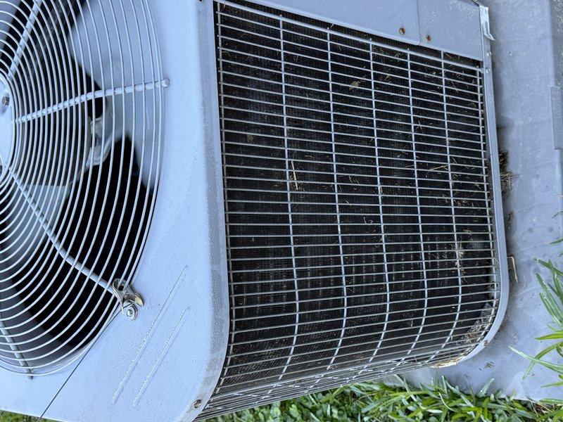 Performed a Service Agreement maintenance visit on the heating and cooling system, connecting a digital manifold gauge set to the outdoor condenser to check refrigerant pressures and overall system performance. Inspected the condenser and found the coil heavily fouled with dirt, grass clippings, and leaf debris restricting airflow; cleared the debris from the coil guard and fins to restore proper heat transfer and airflow. Verified the electrical disconnect and fan assembly condition, and confirmed the unit was operating within normal parameters.