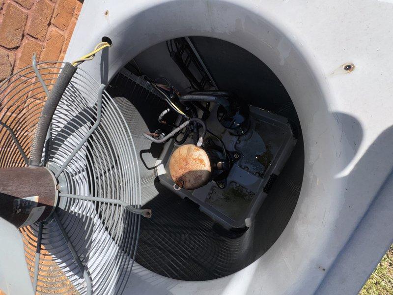 Performed a service agreement visit on the outdoor condensing unit, removing the fan guard to inspect the interior components. Found heavy rust and corrosion on the compressor, along with debris buildup, staining, and standing moisture in the base pan, and documented the condition with photos. Verified the unit's condition under warranty coverage and noted that no UV light was installed on the system.