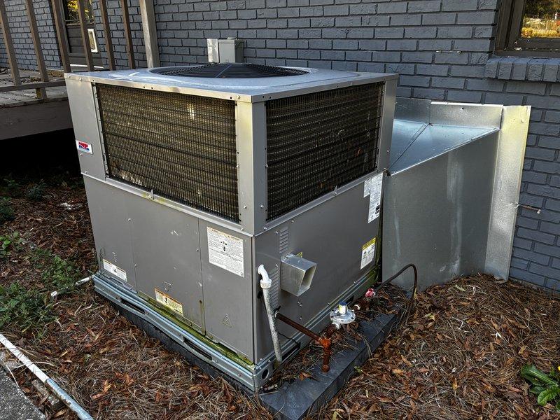 Completed a Protection Visit on the outdoor packaged HVAC unit, inspecting the cabinet, coil guards, access panels, electrical disconnect, gas line with shutoff valve, condensate drain line, and duct transition. Unit was found structurally sound with no rust, frost, or visible damage; minor algae/mildew growth was noted along the base frame, and pine straw and leaf debris were present around the pad. Recommend clearing debris from the unit perimeter to maintain proper airflow and prevent moisture buildup.