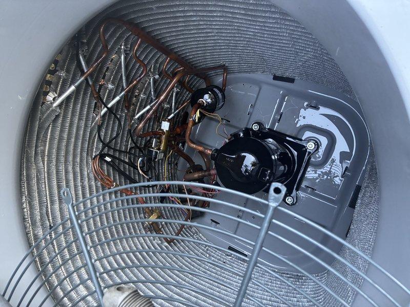Performed a first service agreement visit on the heat pump system, including inspection of the outdoor condenser unit with the top section removed for access to the fan assembly, condenser coil, compressor, and refrigerant line set. Cleaned the condenser coil with a brush to remove debris and restore airflow, and noted frost accumulation around the unit consistent with cold-weather heat pump operation. Observed oily residue pooled on the compressor base plate near the refrigerant fittings, indicating a possible refrigerant or oil leak that warrants further leak testing and evaluation.