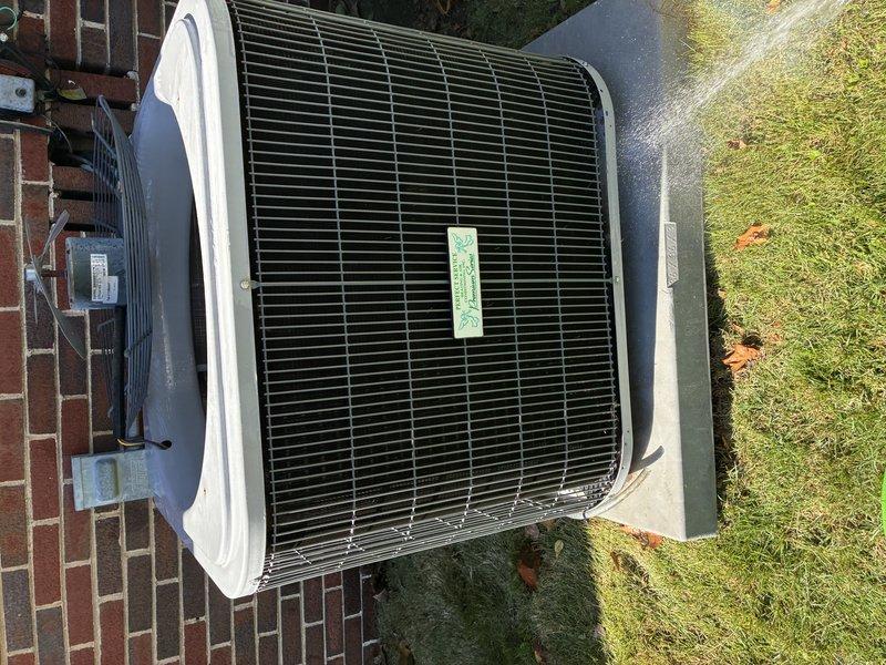 Performed a service agreement visit on the outdoor condenser unit, removing the fan assembly and guard to access the interior components. Inspected the condenser coil fins, compressor, refrigerant line set, capacitor, and electrical wiring and terminals, and washed the coil and cabinet to clear accumulated dirt and debris. Noted surface corrosion on the compressor shell and moisture and frost-like buildup on the base pan, which should be monitored at future visits.