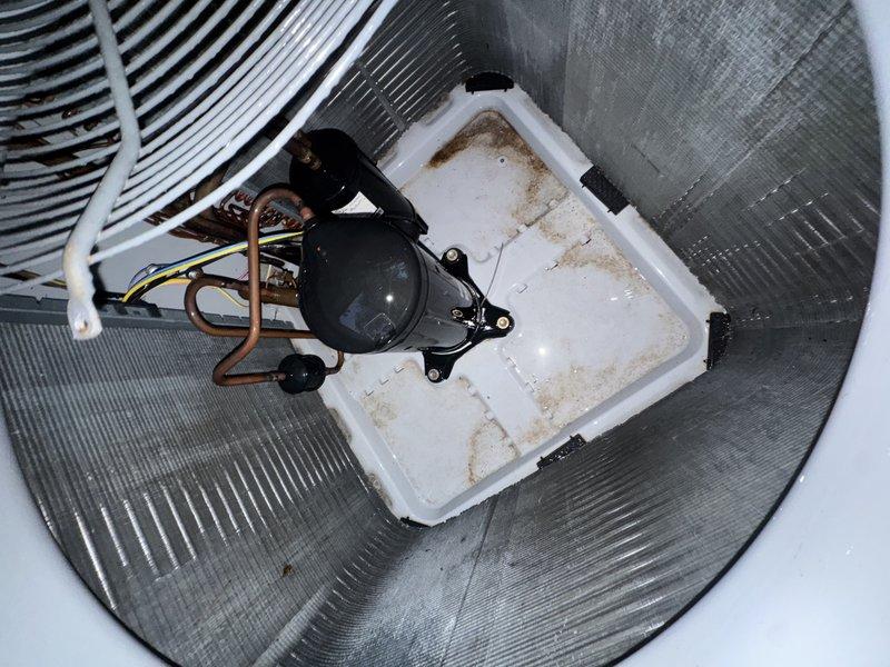 Performed a service agreement inspection of the outdoor condensing unit, including evaluation of the condenser coil, scroll compressor, fan assembly, copper refrigerant lines, and electrical wiring. Observed heavy dust and grime accumulation on the aluminum coil fins and a buildup of leaves and debris in the base pan, with staining and residue on the pan surface. Documented unit condition with photos and cleared debris from the cabinet interior to restore proper airflow and drainage, with coil cleaning recommended to maintain heat transfer efficiency and system performance.